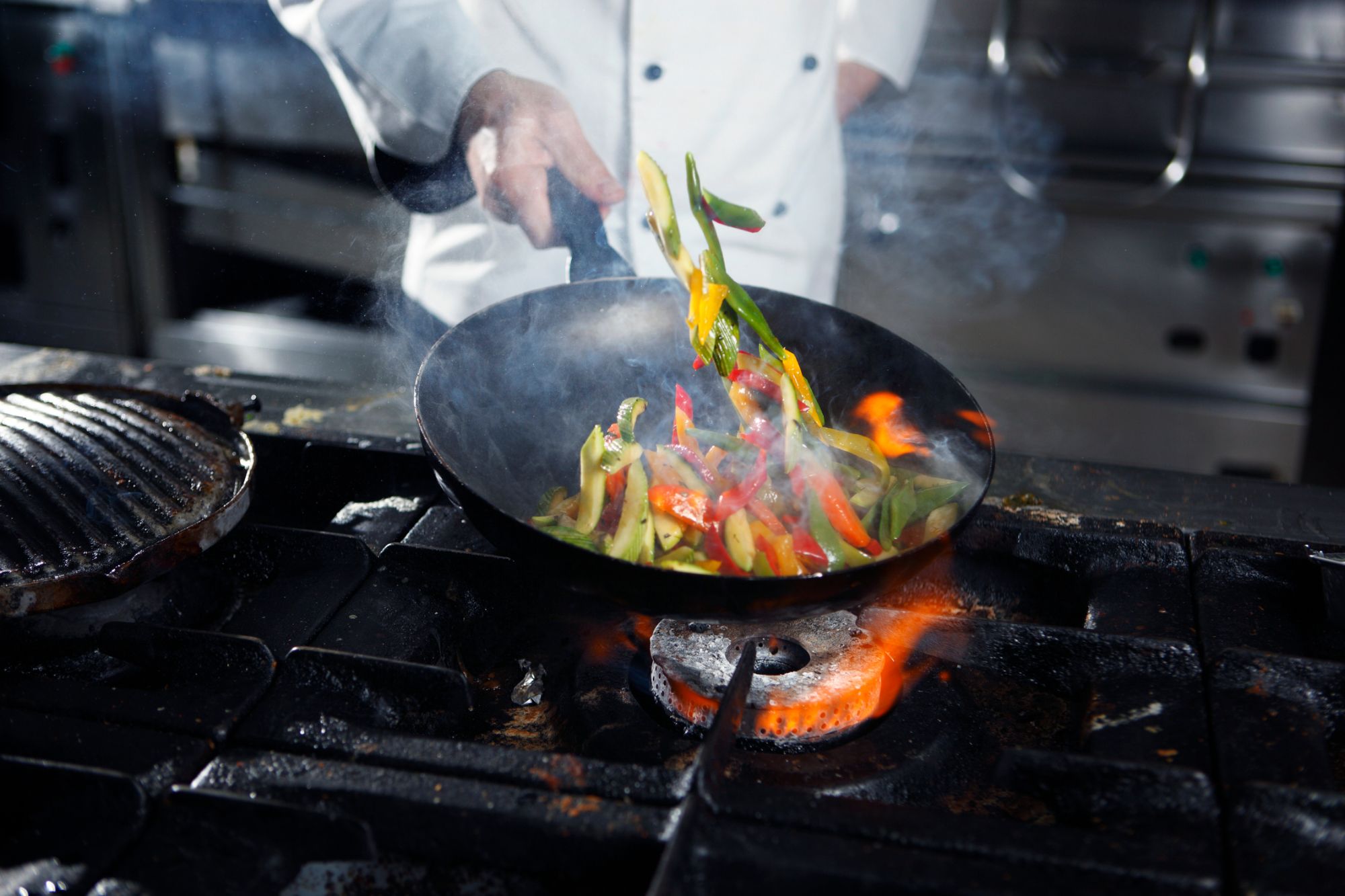 Cook working a flaming wok on the line during dinner service